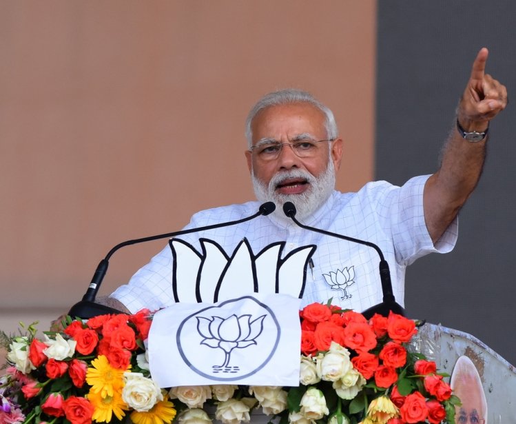 A photo of Prime Minister Narendra Modi at a podium with a raised arm addressing BJP.
