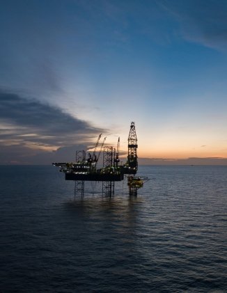 An offshore oil rig in the ocean at sunset.