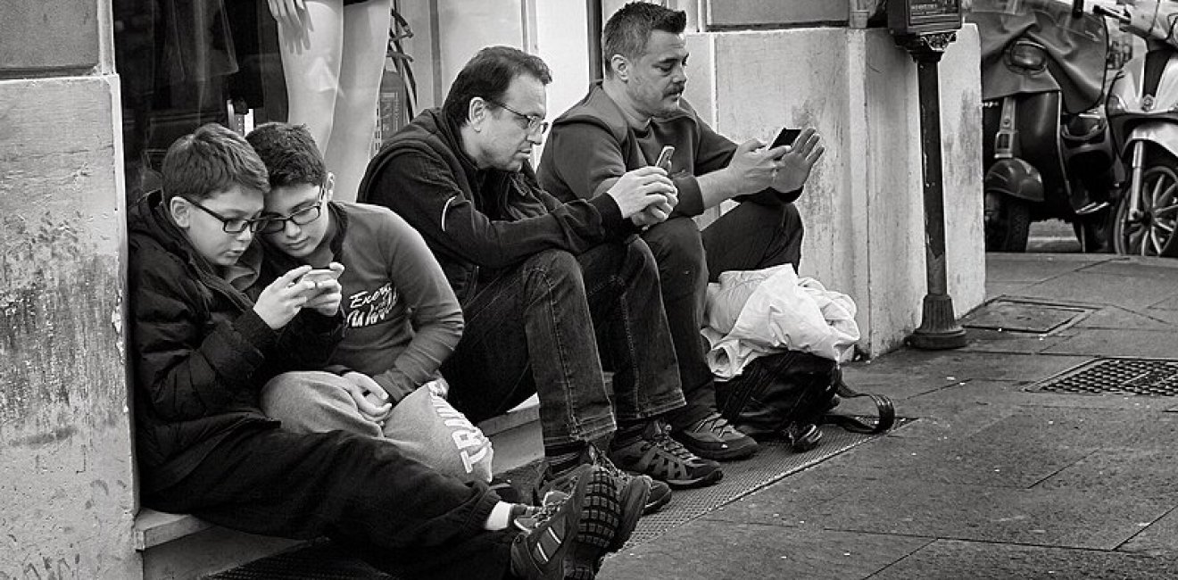 People holding smart phones while sitting. Source: Wikimedia Commons.