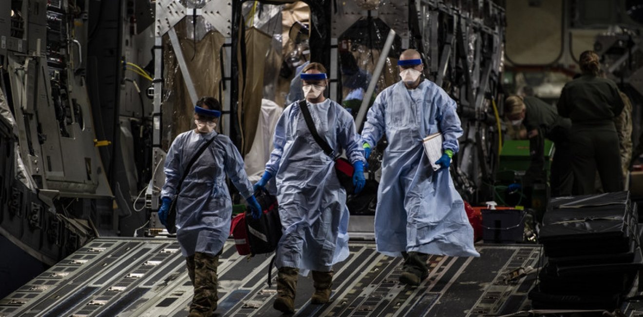 Three U.S. Air Force medical Airmen exit a C-17 Globemaster III following the first-ever operational use of the Transport Isolation System at Ramstein Air Base, Germany, April 10, 2020. The TIS is an infectious disease containment unit designed to minimize contamination risk to aircrew and medical attendants, while allowing in-flight medical care for patients afflicted by a disease—in this case, COVID-19.
