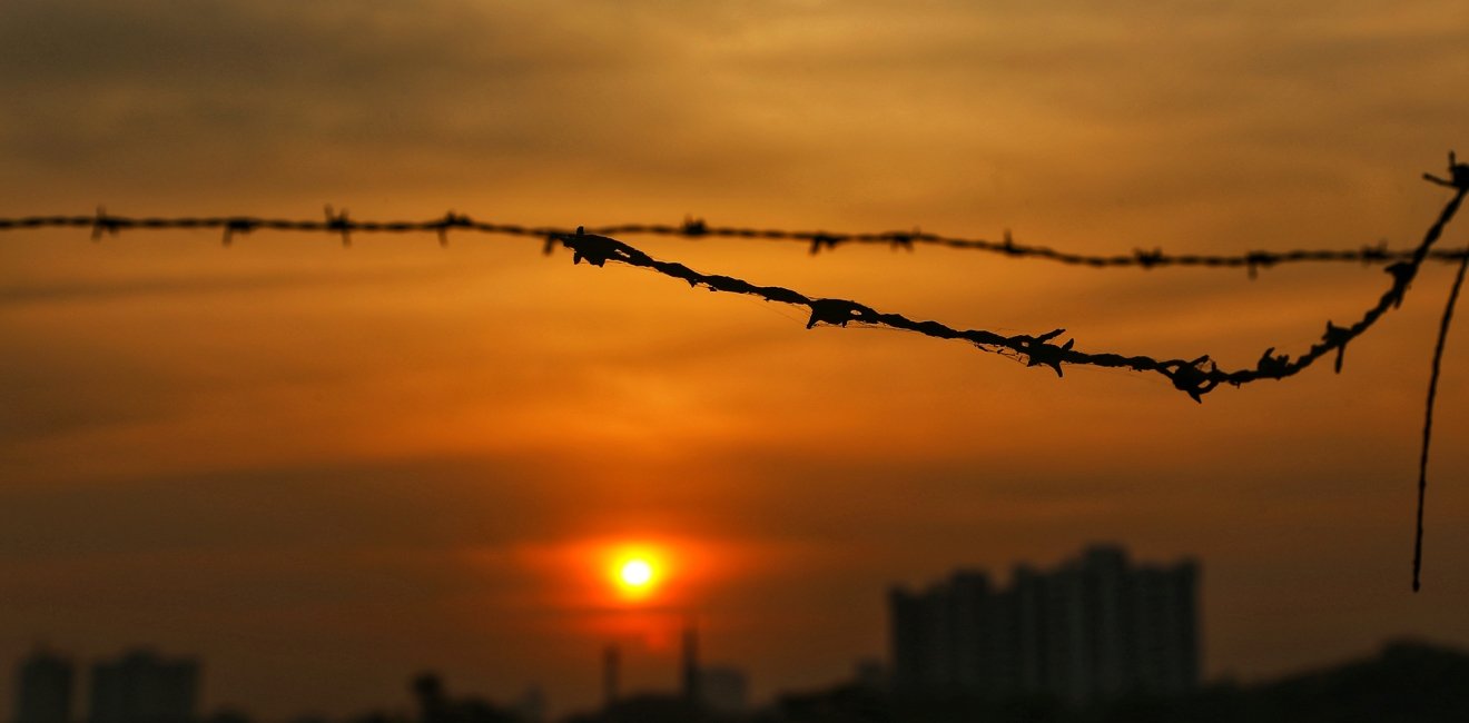 A piece of barbed wire in the foreground of a sunset over Mumbai