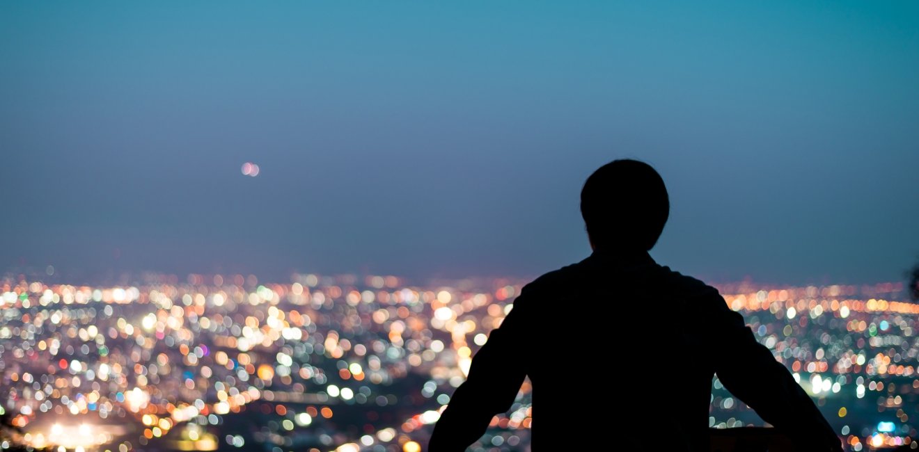 A man looking out at a city skyline at night.