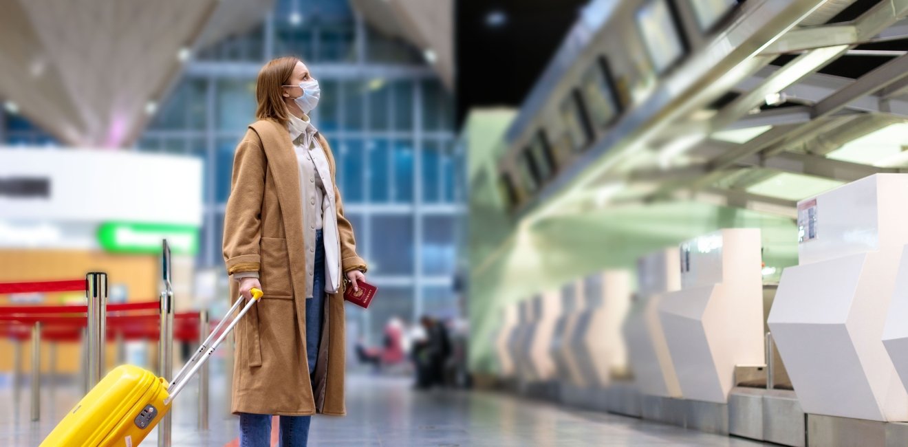 Woman with luggage stands at almost empty check-in counters at the airport terminal due to coronavirus pandemic/Covid-19 outbreak travel restrictions. Flight cancellation. Quarantine all over the world