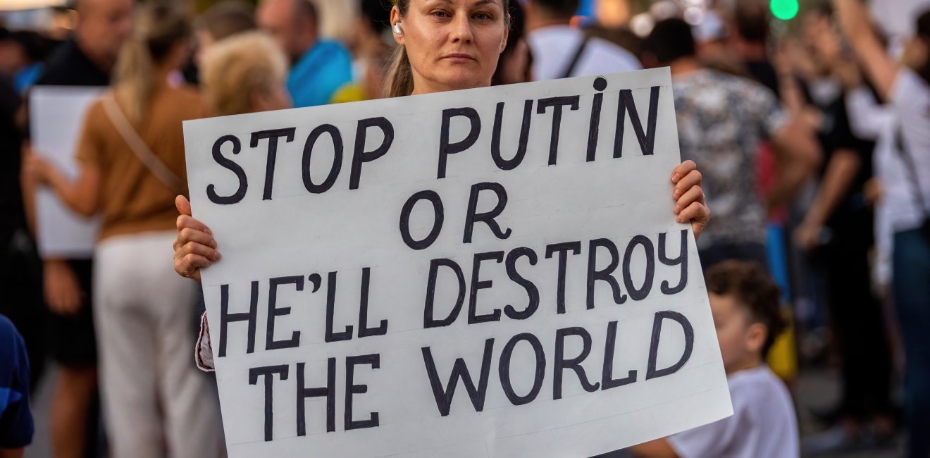 Woman holds a protest sign reading "stop Putin or he'll destroy the world"