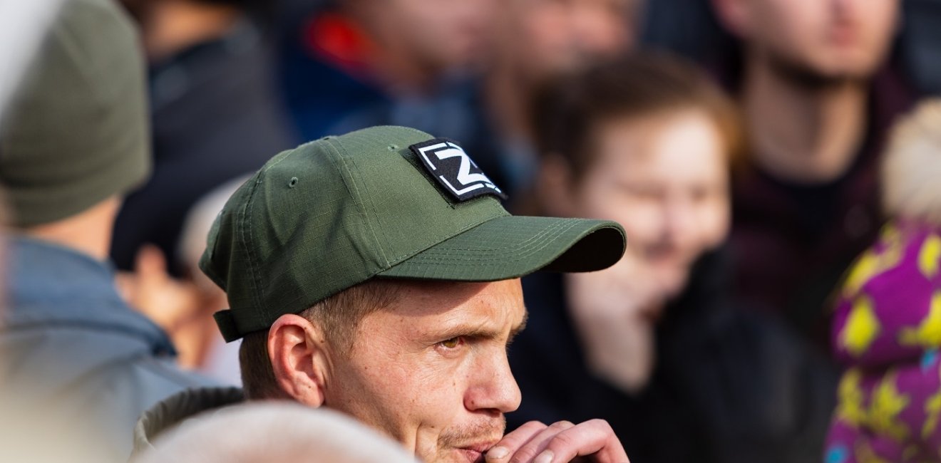 Man in crowd smoking a cigarette and wearing a hat in support of the special military operation