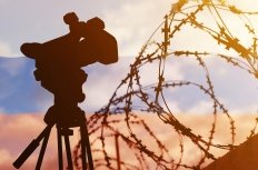 A composite photo with the Russian flag in the background, and barbed wire and a television news camera in the foreground