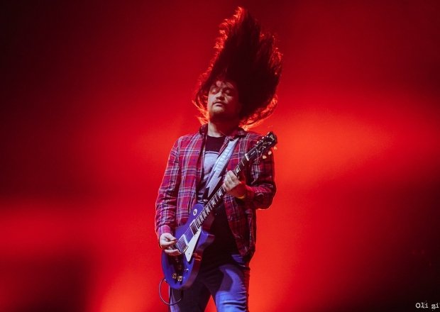 Man on stage whipping hair and playing the guitar