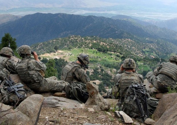 Five U.S. soldiers sit on a ridge looking out at a valley in Afghanistan.