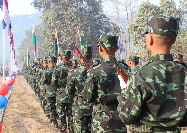 A line of men in camouflage face away from the camera.