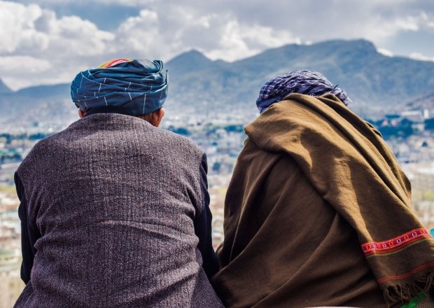 Two men sit with their backs to the camera, looking out at the Afghan mountains.