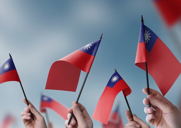 A close up of hands waving small Taiwanese flags.