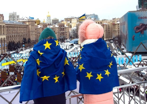 Two people overlooking square with EU flags on their backs
