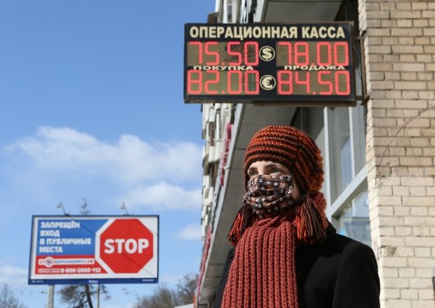 A woman stands in front of a sign displaying the ruble's exchange rate
