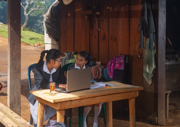 Two girls sitting in front of a computer in the rural outdoors.