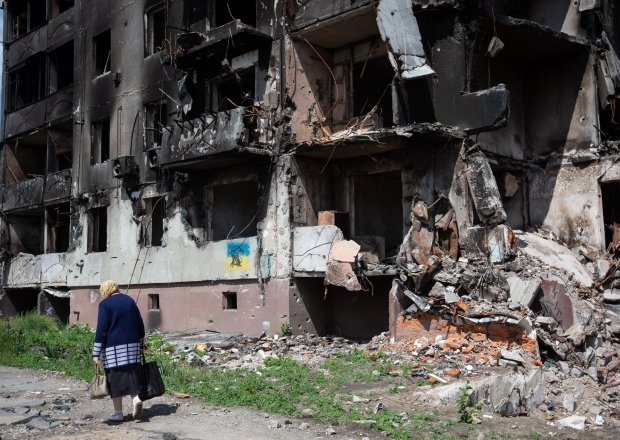 old woman walks past apartment building destroyed by the Russian army as a result of Russia's invasion of Ukraine in Borodianka, Ukraine