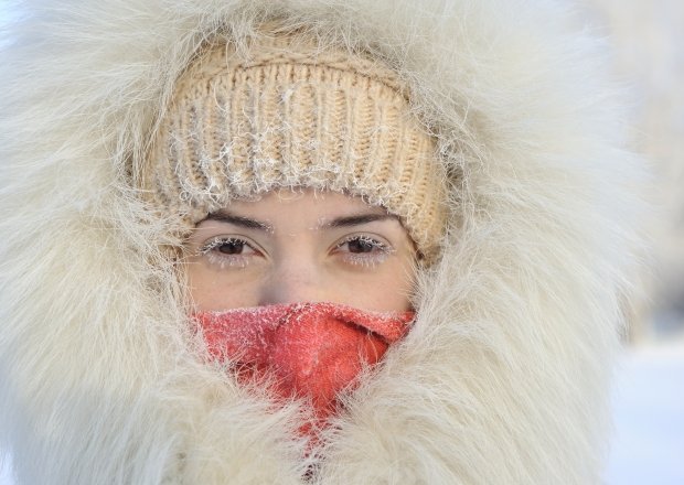 Girl with hoarfrost on the eyes. The white fur coat and hood. Very cold, frost.