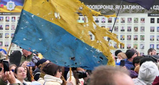 a tattered Ukrainian flag flies above a crowd of people