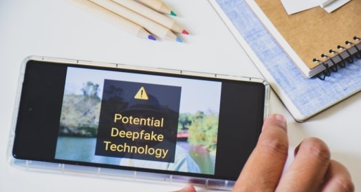 A phone with a picture in the background displaying the warning: potential deepfake technology 