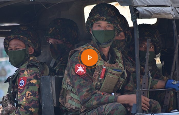 A group of soldiers wearing fatigues and facemasks in the back of a military vehicle.