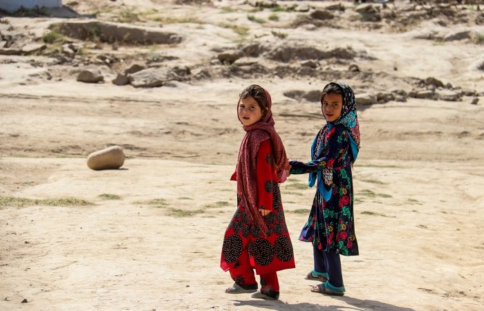 Two young children standing, facing away from the camera, in a desert environment.