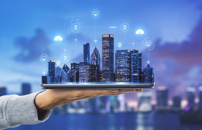 Smart city technologies concept with digital tablet and night megapolis city skyscrapers with digital cloud icons on human hand at blurry skyline background