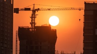 The setting sun illuminates a large tower and construction crane.