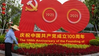 A gardener waters plants in front of a CCP at 100th installation