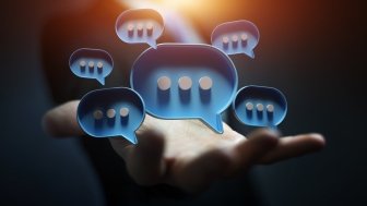 Businessman in dark using digital blue speech bubbles talk icons. Minimal conversation or social media messages floating over user hand. 3D rendering