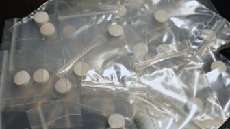 Table of drug dealer with fentanyl pills in pressed powder packed in small bag, heroin and methamphetamines, illicit drugs. Dangerous fentanyl and money bill evidence at a crime scene.