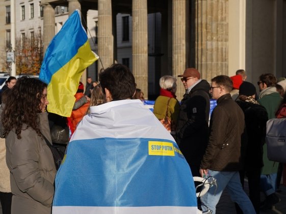 Berlin, Germany - November 13, 2022: Male demonstrator covered with a white-blue-white flag at a rally in solidarity with Ukraine against Russian Imperialism at Brandenburg Gate in Berlin