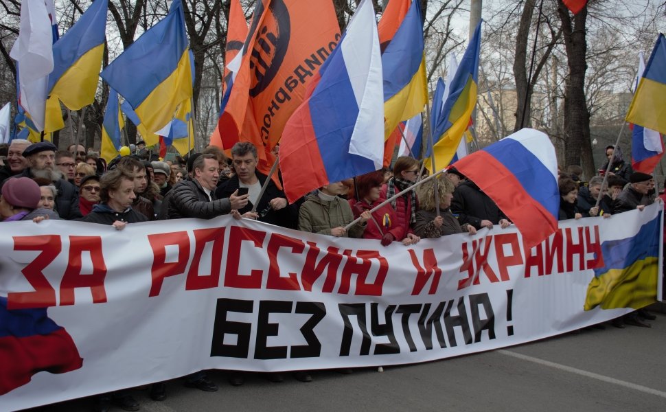 Boris Nemtsov stands at a protest holding a banner reading "For Russia and Ukraine Without Putin" in 2014.