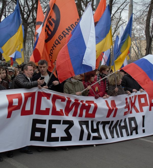 Boris Nemtsov stands at a protest holding a banner reading "For Russia and Ukraine Without Putin" in 2014.