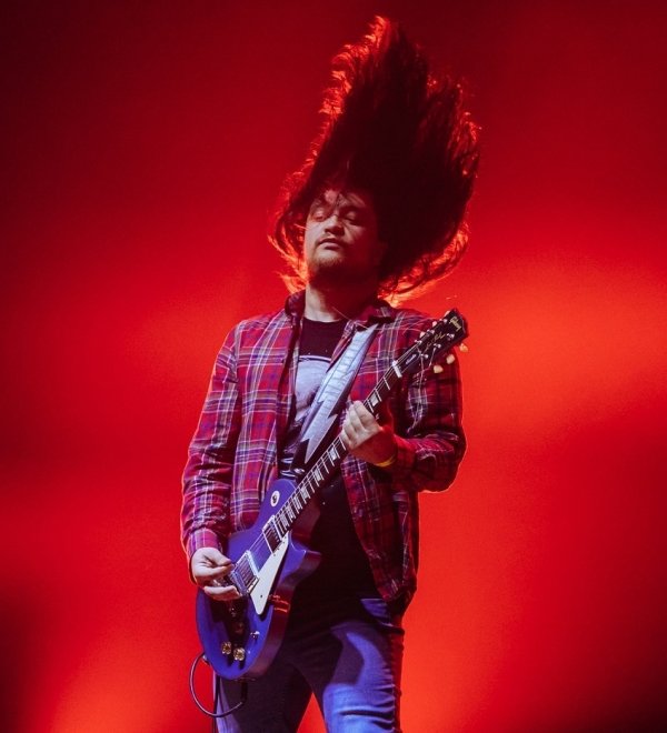 Man on stage whipping hair and playing the guitar