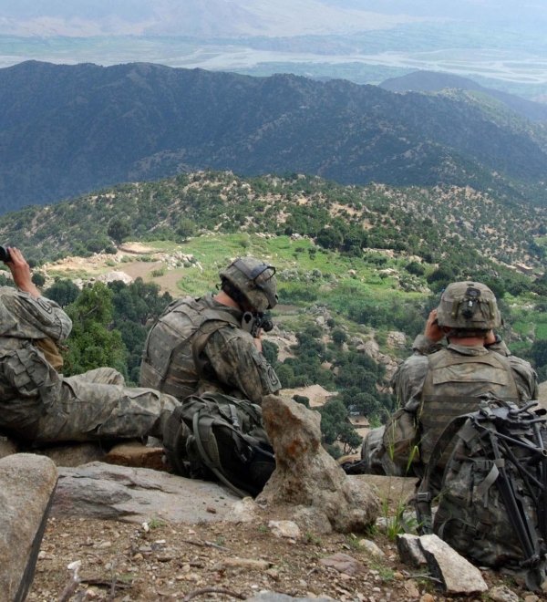 Five U.S. soldiers sit on a ridge looking out at a valley in Afghanistan.