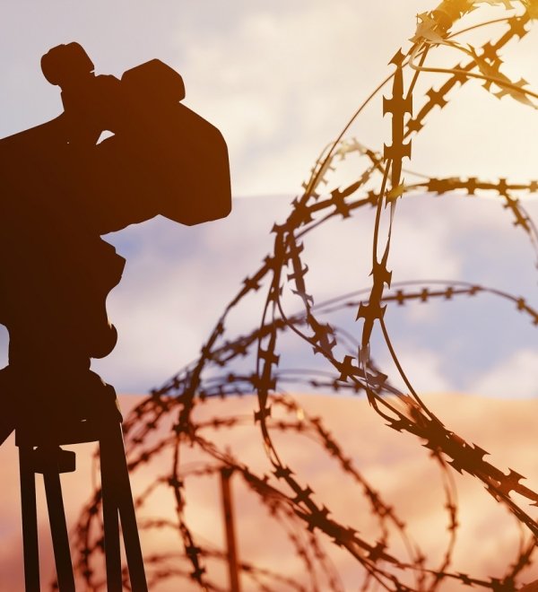 A composite photo with the Russian flag in the background, and barbed wire and a television news camera in the foreground