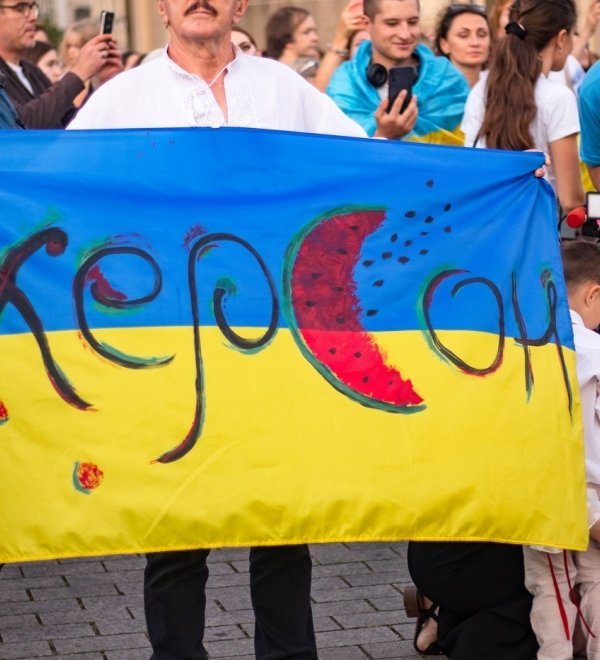 Person holding Ukrainian flag with text "Kherson" and watermelon motifs