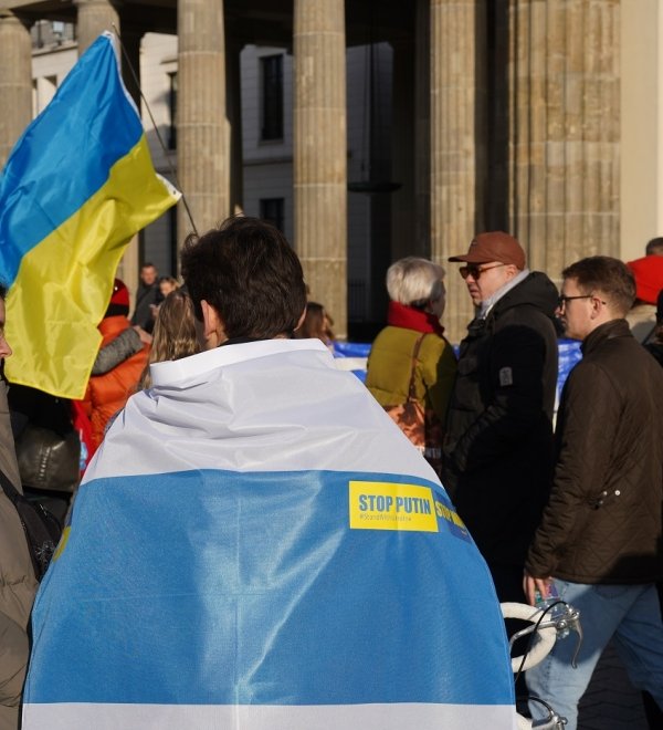 Berlin, Germany - November 13, 2022: Male demonstrator covered with a white-blue-white flag at a rally in solidarity with Ukraine against Russian Imperialism at Brandenburg Gate in Berlin