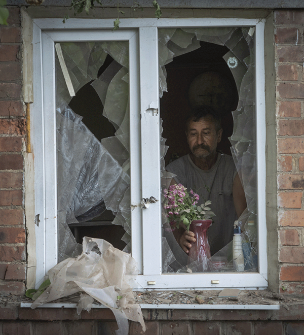 A local resident places a vase with flowers on a broken window in his house damaged by the Russian shelling in Bakhmut, Donetsk region, Ukraine. June 26, 2022. AP Photo/Efrem Lukatsky.