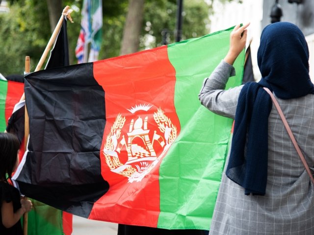 Two people with their backs to the camera are holding a large Afghan flag.