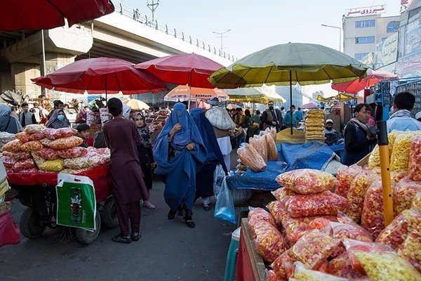 Afghan men and women in traditional clothing shop at an outdoor market.
