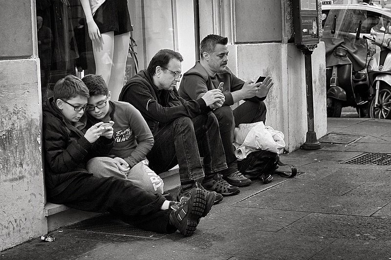 People holding smart phones while sitting. Source: Wikimedia Commons.