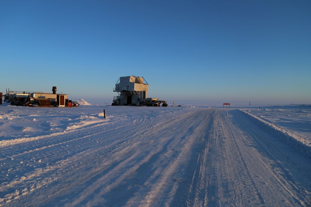 Snow road with a substructure of the oil work over rig and a distant view of the drilling rig at an oilfield in the tundra in winter. Source: Shutterstock