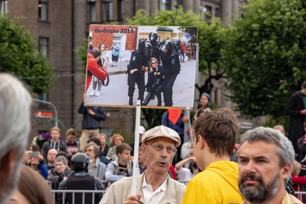 An elderly man holds a banner at a rally with a photo of opposition politician Lyubov Sobol being detained. Source: Shutterstock.