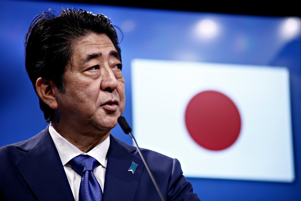 Prime Minister Shinzo Abe speaks in front of a Japanese flag at an event.