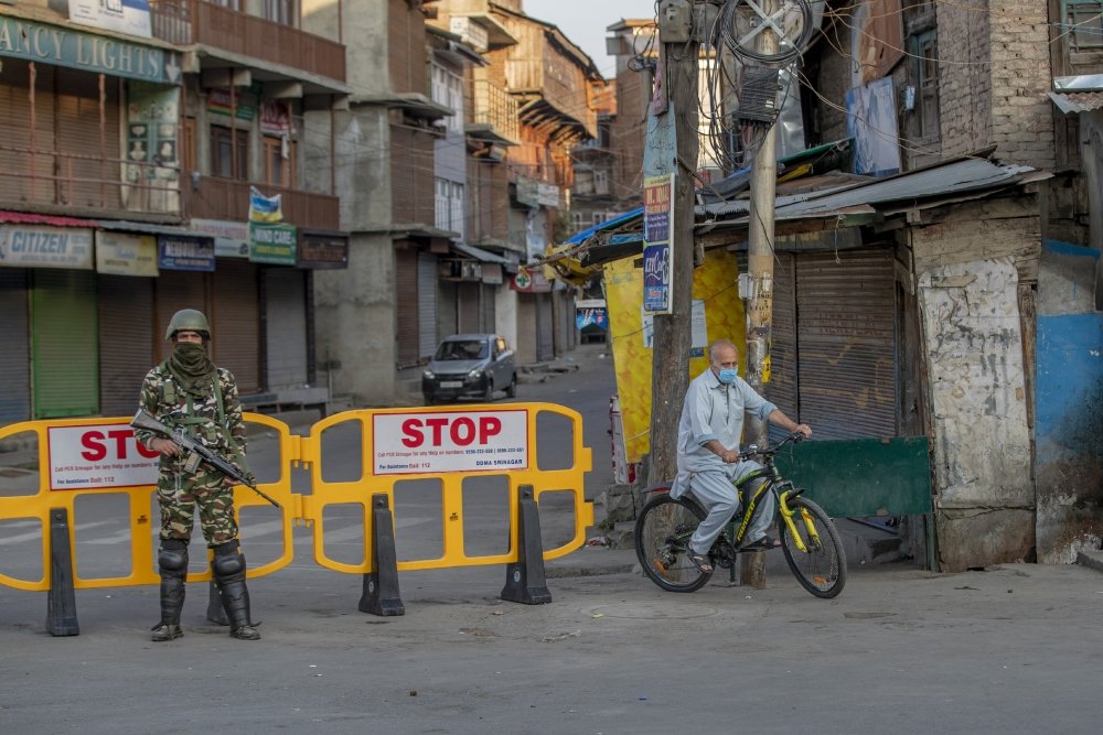 A Kasmiri man on a bicycle rides past a barricade guarded by a soldier.