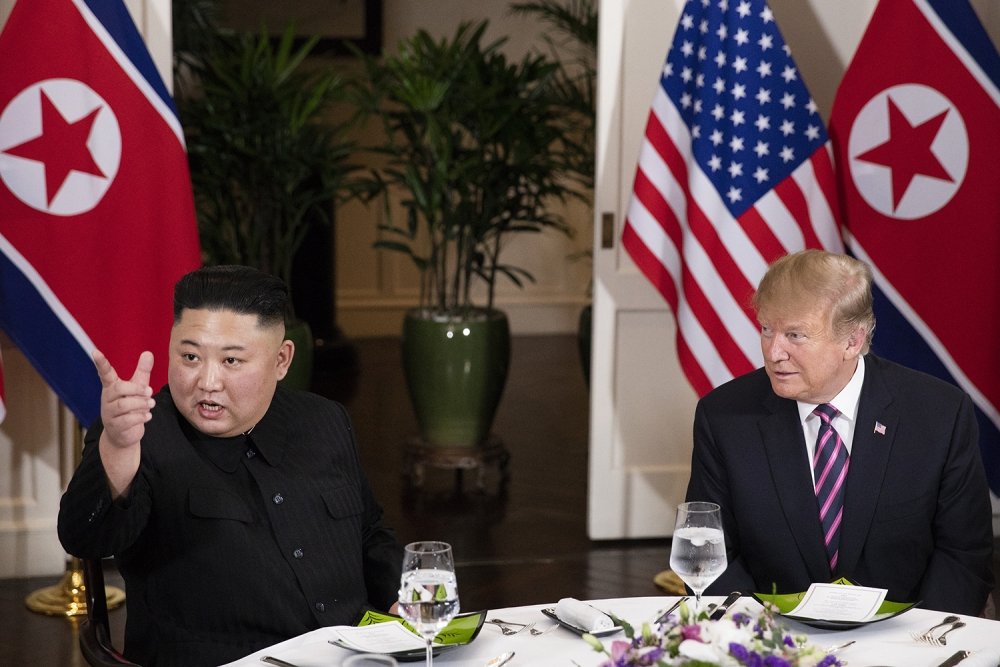 Kim Jong Un sits at a dinner table next to Donald J. Trump