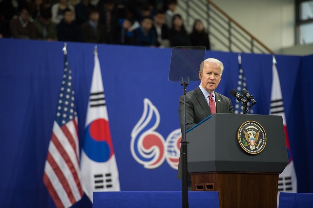 Joe Biden stands at a podium delivering a speech in front of U.S. and South Korean flags