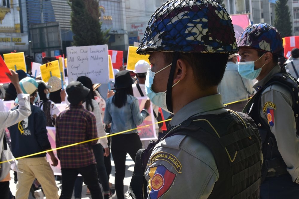 Two soldiers in miliary uniform watch a crowd of protestors.