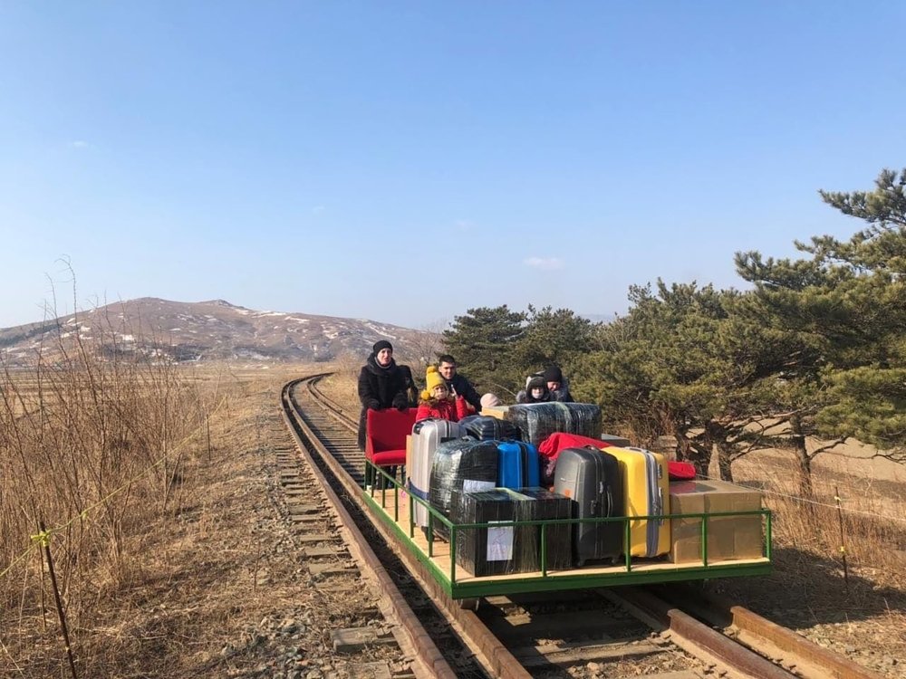 A group of people hand pushing a small railway cart loaded with lugagge.