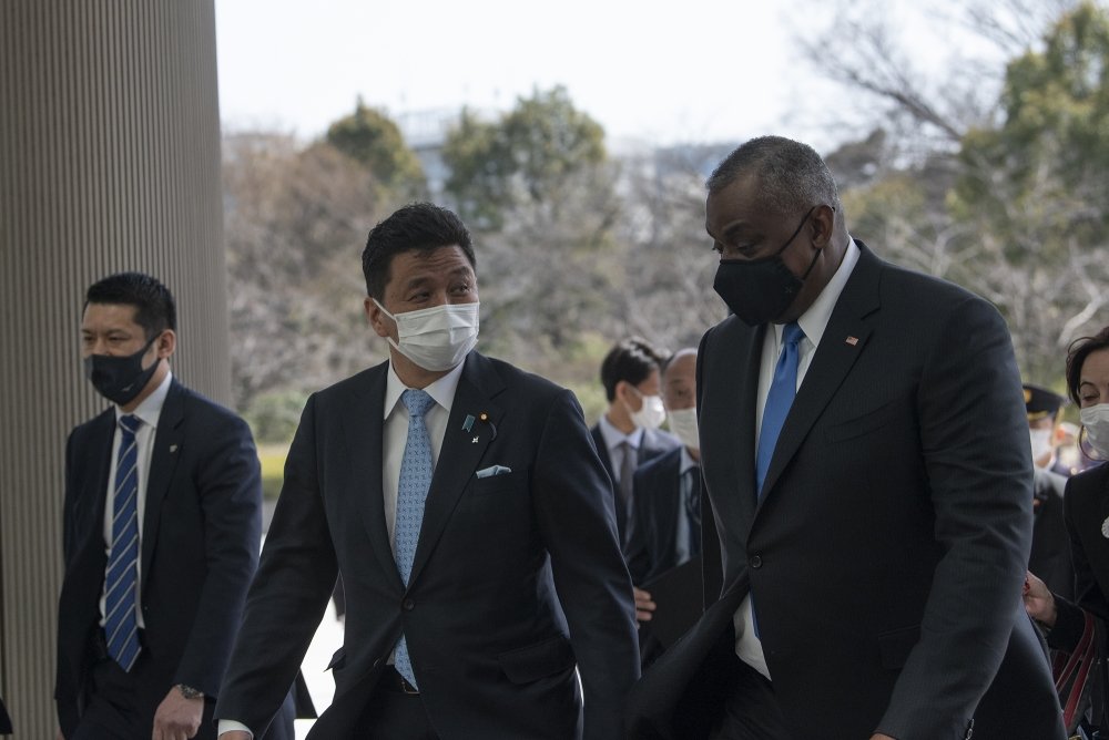 A group of men wearing medical masks talk as they they are walking into a building.